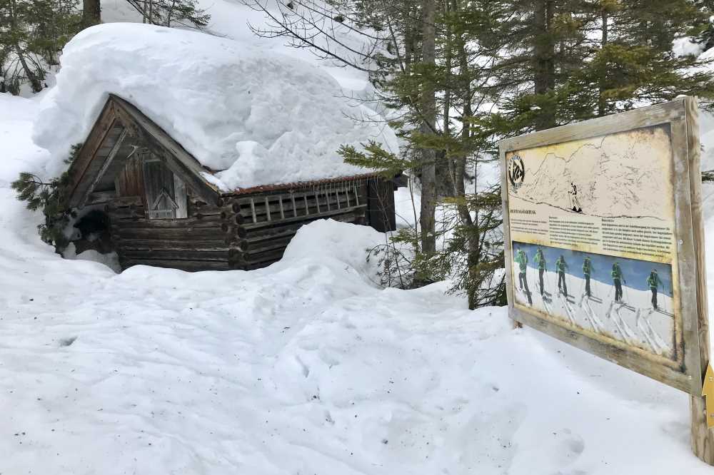 Auf dem Weg zum Gipfel komme ich bei dieser verschneiten Hütte und der Tafel des Skitourenlehrpfads vorbei
